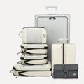 Cube Packer Travel System Bundle in Cream including compression packing cubes, shoe bag, laundry bag and toiletries bag arranged in front of a suitcase
