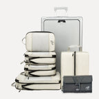 Cube Packer Travel System Bundle in Cream including compression packing cubes, shoe bag, laundry bag and toiletries bag arranged in front of a suitcase
