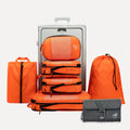 Cube Packer Travel System Bundle in Orange including packing cubes, shoe bag, laundry bag and toiletries bag arranged in front of a suitcase