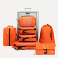 Cube Packer Travel System Bundle in Orange including compression packing cubes, shoe bag, laundry bag and toiletries bag arranged in front of a suitcase