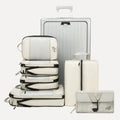 Cube Packer Travel System Bundle in Cream including compression packing cubes, shoe bag, laundry bag and toiletries bag arranged in front of a suitcase
